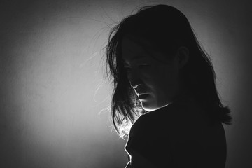 silhouette of depress woman standing in the dark with light shine behind