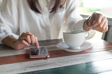 front view. woman playing mobile phone while brew coffee in morning time. front of her having coffee cup putting on wooden table. this image for business, technology, beverage and portrait concept
