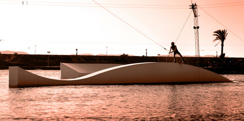 Wakeboarding sportsma sliding wakeboard on the slider in the wake cablepark, sunset session,...