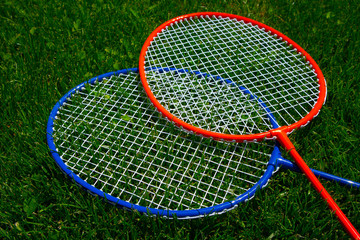 Two badminton racket on the sunny bright grass green fresh background. Photo depicts two colorful shuttlecock rackets in the garden, funny game competition start concept. Closeup, macro view.