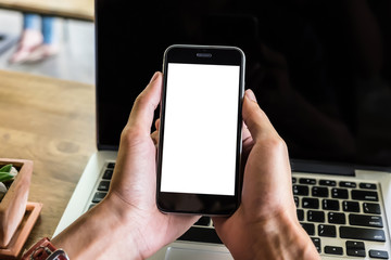 Close up hand holding smart phone and use laptop on ther wood desk in coffee shop. vintage effect. .Smart phone with blank screen and can be add your texts or others on smart phone.