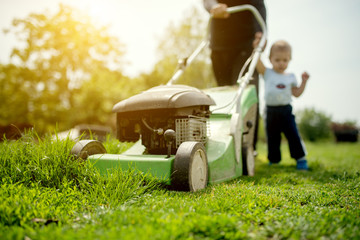Baby boy and his grandfather mowing the grass with lawnmower. Arranging their garden on a summer...