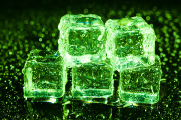 Ice cubes in green light on black wet table.