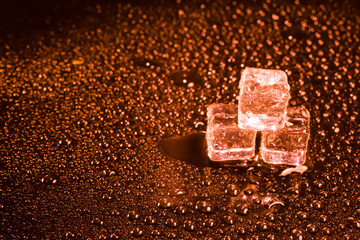 Ice cubes in red light on black wet table.
