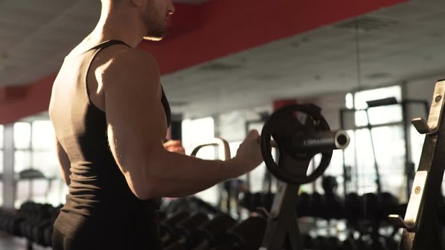 Attractive and self-confident man pumping muscles at gym, looking at reflection