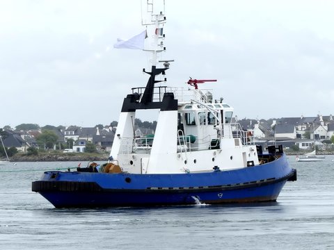 Blue and white Tug Boat in operations  at Lorient harbor, France. Horizontal  three-quarter stern view.