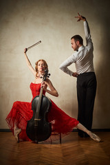 Female ballet dancer in red dress and pointe playing on antique black cello and male dancing latin