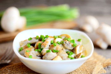 Fried mushrooms with sour cream and fresh green onions in a bowl. Vegetarian food. Easy healthy mushrooms recipe. Fresh mushrooms, green onions, fork on old wooden table. Closeup
