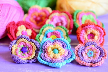 Vivid crochet flowers on purple wooden background. Crocheted flowers from colourful cotton yarn. Easy summer handmade crafts idea. Closeup