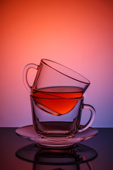 Two cups and saucers of glass. Tea is poured into the top Cup. Helium filter gives a beautiful light. Studio photos using the backlight. The reflection on the black table. The background is blue-red.