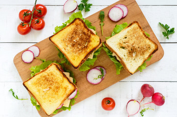 Fototapeta na wymiar Multilayered sandwiches with a juicy cutlet, cheese, radish, cucumber, lettuce, arugula on a cutting board on a white wooden background. Top view.