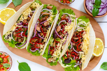 Tacos is a traditional Mexican dish. Tortilla stuffed with chicken, bell and hot peppers, beans, lettuce, cheese, blue onion with salsa sauce on white wooden background. Top view. Close up