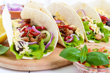 Tacos is a traditional Mexican dish. Tortilla stuffed with chicken, bell and hot peppers, beans, lettuce, cheese, blue onion with salsa sauce on white wooden background.