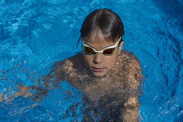 Naklejka premium Boy with swimming goggles in pool, above view. Blue water background.