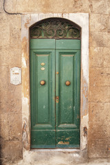 The old shabby door is green on the wall of the old stone house..