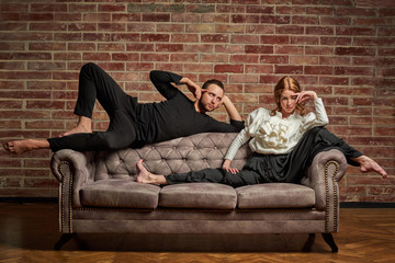 Female ballet dancer and male latin dancer in contemporary style in pose lie on the sofa