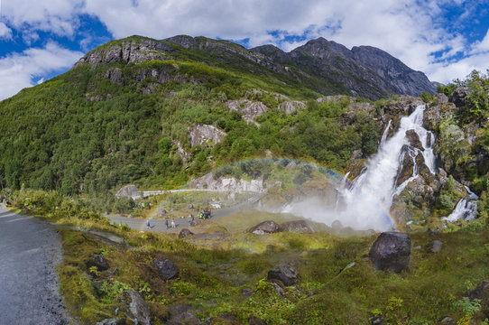 Waterfall in Briksdalbreen Glacier valley. Tourist on the trail. 