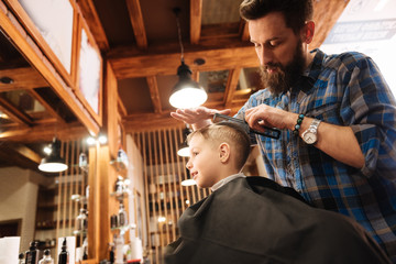 Nice bearded hairdresser using his instruments