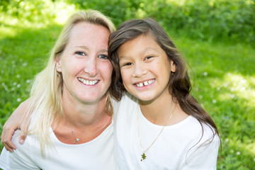 daughter makes a hug to her mother sitting in the green grass