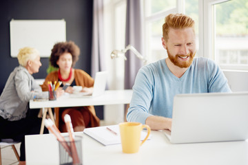 Fototapeta premium Caucasian businessman sitting in modern office and using laptop. colleagues in background
