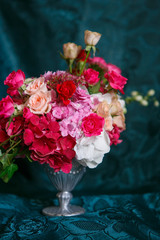 An asymmetric bouquet in a vase of roses, carnations and hydrangeas on a dark blue background