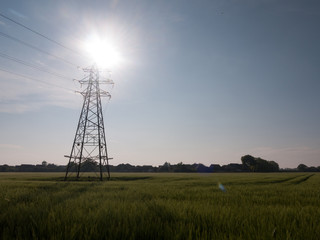 an electric pylon outside with sun behind it over field communication