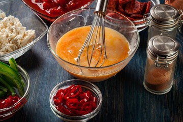Ingredients for preparing frittata - eggs, sausage chorizo, red pepper, green pepper, tomatoes, chili and cheese on wooden table
