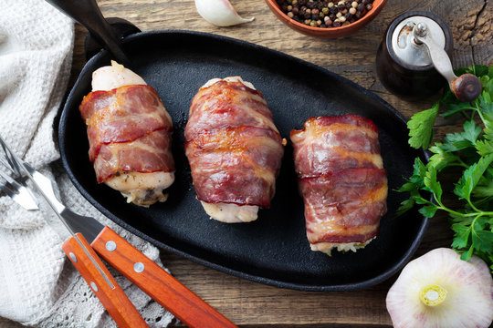 Baked chicken breast wrapped in bacon on a cast-iron frying pan on an old wooden  background. Selective focus. Top view. Copy space.