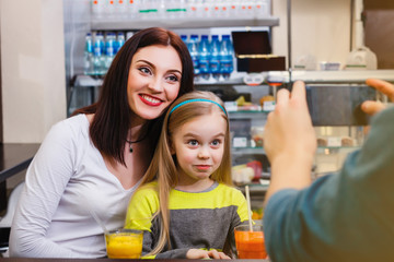 A man makes picture of young mother with her little dauther at a table in a cafe