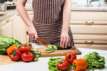 Young woman cooking in the kitchen at home. A woman cuts a cucumber and vegetables with a knife.