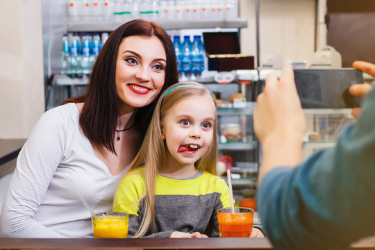 A man makes picture of young mother with her little dauther at a table in a cafe
