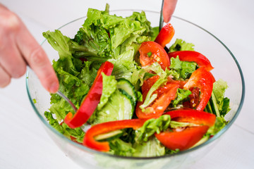 Young woman dressing vegetable salad with olive oil on a white background