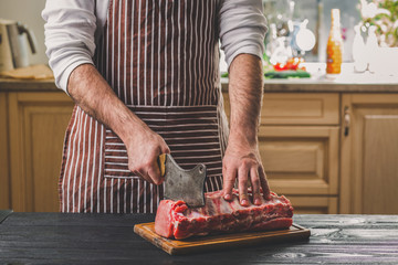 Man cuts of fresh piece of meat on a wooden cutting board in the home kitchen