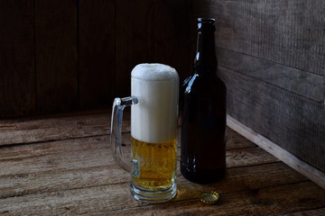 Mug of beer, bottle on wooden background. Photographed with natural light