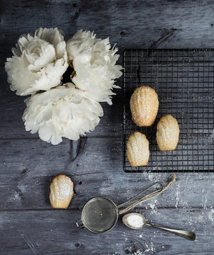 Overhead view of madeleine pastry, white flower and sieve on wooden table
