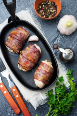 Baked chicken breast wrapped in bacon on a cast-iron frying pan on a black background. Selective focus. Top view. Copy space.