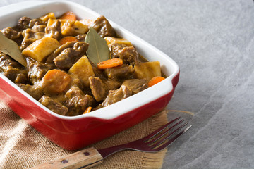 Beef meat stewed with potatoes, carrots and spices in ceramic pot on gray stone
