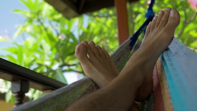 Swinging bare man feets in a hammock on terrace. Vacation on Koh Tao Tanote Bay, Thailand