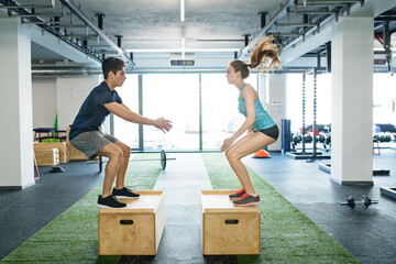 Young fit couple exercising in gym, doing box jumps.