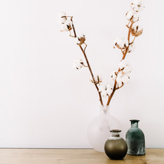 Front view of cotton branches and beauty stylish vase at white background. Minimalistic decorated home office desk.