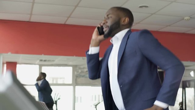 Successful businessman running on treadmill and talking on cellphone at the gym