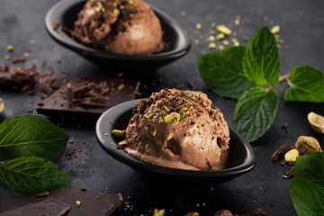 Tasty appetizing chocolate ice cream with mint and pistachios in small cup on dark background. Horizontal with copy space.