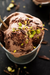 Tasty appetizing creamy chocolate ice cream with pistachios in small metal cup on dark background. Closeup.