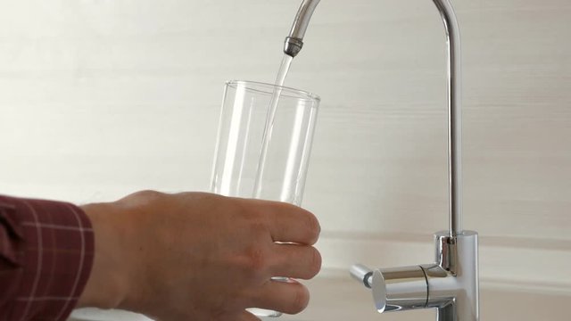 Man filling glass of water from kitchen faucet