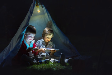 Cute little brothers, playing on tablet and telephone at night in campside