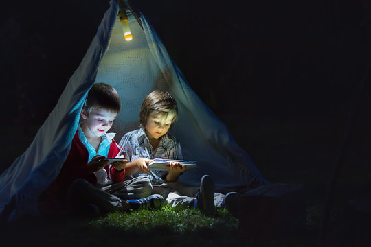 Cute Little Brothers, Playing On Tablet And Telephone At Night In Campside