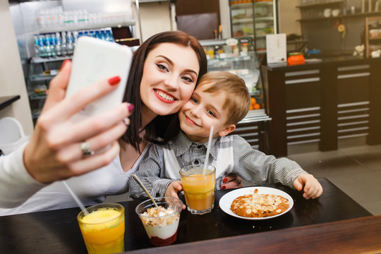 A young mother makes selfie with her little son at a table in a cafe