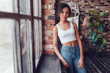 Beautiful african girl in white top standing near the window.