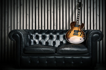 empty vintage sofa and electric guitar with modern wood wall recording studio background. Music...