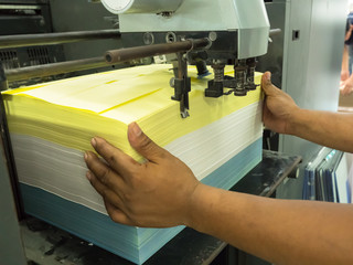 Close up on worker hand while offet printing machine feeding the paper into the system
